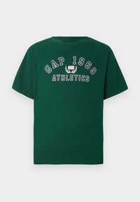 Mork grøn t-skjorte i bomull med hvit tekst "GAP 1969" og "ATHLETICS", samt et lite amerikansk flagg og laurbærgrafikk. Klassisk passform.