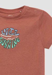 Kastanjebruin babyshirt met korte mouwen, drukknoopjes op de schouder en een cartoon krokodil met de tekst "LITTLE SUNSHINE" in blauw en groen.