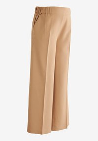 Pantalons larges beiges avec une texture lisse, une taille élastique, des poches latérales et des lignes épurées, présentant un design soigné.