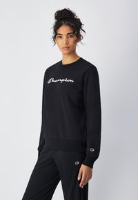 Felpa nera in cotone, con collo rotondo, maniche lunghe e il logo "Champion" ricamato in bianco sul petto.