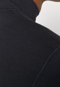 Suéter de cuello alto de punto acanalado en color navy, con una textura suave, que presenta un cuello alto y costuras detalladas a lo largo de las costuras.