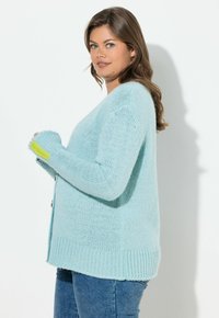 Světlomodrý pletený kardigan s volným střihem, žebrovaným lemem a zářezy na palce v jasně zelené barvě na rukávech.