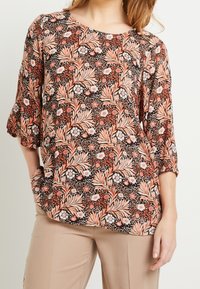 Blouse multicolore avec des motifs floraux et de feuilles dans des nuances de corail, blanc et noir. Encolure ronde et manches trois-quarts. Tissu doux.