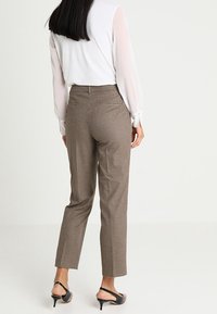 Bruna rutiga byxor har en smal passform med en flat front och bakfickor. Kombineras med en vit långärmad blus och svarta klackar.