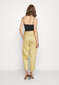 Haut noir à bretelles, pantalon taille haute beige avec détails volants à la taille, et sandales à talons noires. Tissu doux, coupe décontractée.