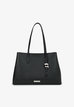 Crna kožna torba s dvostrukim trakama i privjeskom u obliku stiliziranog lica koje nosi sunčane naočale.