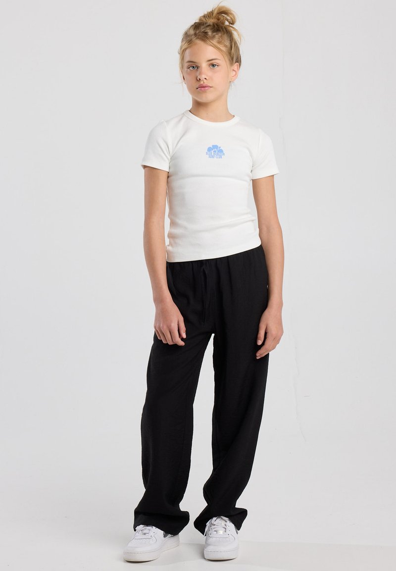 White ribbed t-shirt with blue graphic, paired with loose black pants and white sneakers, featuring a simple, casual design.
