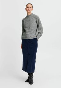 Gray knit sweater with high collar, ribbed texture, and dropped shoulders, paired with a navy corduroy midi skirt and knee-high black boots.