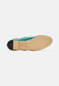 Zapato de charol en color verde azulado con punta afilada, textura suave y tacón de cuero negro. Suela beige con detalles en relieve y talla 37.