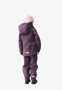 Veste à capuche violette avec taille élastique, associée à un pantalon assorti. Le matériau est lisse, et un bonnet en tricot crème vient compléter l'ensemble.