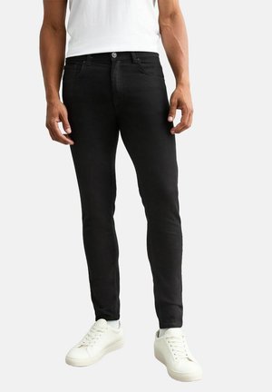 Schwarze Skinny Jeans aus Denim, mit fünf Taschen und Knopfverschluss, kombiniert mit weißen Sneakers und einem weißen T-Shirt.