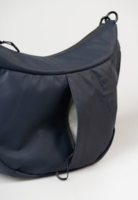 Borsa a spalla blu navy realizzata in materiale liscio, con una tasca con zip con interno verde e una superficie esterna texturizzata.