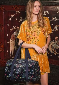 Verižna torba iz temno modrega barvila z cvetličnim vzorcem, izdelana iz močnega žameta, z trpežnimi mornarsko modrimi ročaji in teksturirano površino, ki vsebuje barvite cvetne akcentne elemente.