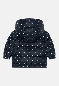 Mustat pehmustetut takki valkoisilla pilkuilla, jossa on huppu, elastiset hihansuut ja bungee-helma. Sileä pinta ja tikattu muotoilu.