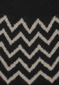 Svart stickad tyg med växelvis tjocka zigzag-ränder i ljusbeige som skapar ett chevron-mönster.