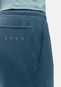 Jogger in cotone blu con una trama liscia, dotato di una tasca sul retro e di un logo discreto sul lato. Vita elastica per il massimo comfort.