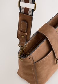 Sac à main en cuir marron avec une bandoulière en tissu rayé réglable, des garnitures en laiton et une ouverture zippée visible.