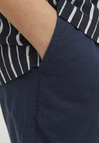 Pantalons en lin bleu marine avec une poche latérale, associés à une chemise rayée avec des rayures horizontales blanches et noires. Gros plan sur le tissu.