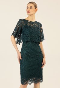 Spitzenkleid in dunklem Teal mit floralem Muster, halbtransparentem Überzug, kurzen Ärmeln und gewelltem Saum. Figurschmeichelnde Silhouette.