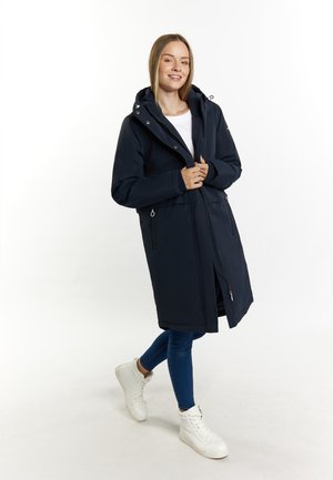 Marineblauwe lange jas met een capuchon, ritssluiting aan de voorkant, zijzakken en een ontspannen pasvorm; gecombineerd met blauwe jeans en witte sneakers.