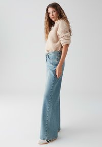 Beige fluffy trui gecombineerd met hoog getailleerde lichtblauwe wijde jeans. De jeans hebben een klassieke vijf-pocket stijl en subtiele vervaging.