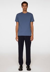 Sininen puuvillainen t-paita, jossa on lyhyet hihat, pyöreä kaula-aukko ja rento istuvuus, yhdistetty tummansinisiin housuihin ja mustiin kenkiin.