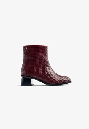 Bottine bordeaux avec une texture tissée et un talon bloc. Présente un bout arrondi et un accent doré près de la cheville.