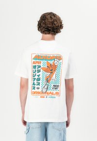 Balts kokvilnas t-krekls ar krāsainu retro grafiku aizmugurē, kas ietver tekstu, varoni un šaha galdiņa akcentus. Brīvs piegriezums.