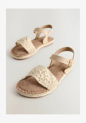 Beige sandaalit, joissa on virkattu hihna, mokkanahkainen pohja ja punottu juuttipohja. Varusteena säädettävä nilkkahihna, jossa on solki.