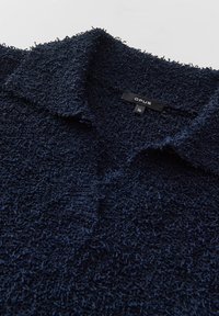 Polo bleu marine en tissu éponge texturé, doté d'un col classique et d'une étiquette avec le nom de la marque et les informations de taille.