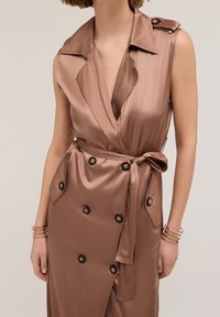 Hnědá saténová bezramínková šaty s překládaným designem, hlubokým V-výstřihem, bočními kapsami, knoflíkovými akcenty a zavazovacími pásky v pase. Hladký povrch.