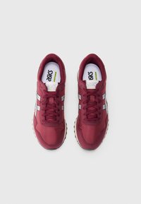 Um par de ténis Asics cor bordeaux com riscas brancas e cinzas vistos de cima sobre um fundo branco.