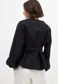 Top peplum negro con mangas largas y cintura anudada, hecho de una tela suave. Presenta un escote amplio y mangas acampanadas.