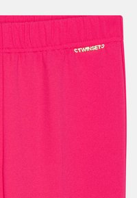 Fuksija legice, izdelane iz raztegljivega materiala z gladko teksturo. Opremljene so z zlatim logotipom "TWINSSET" na pasu.