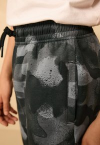 Felpa con stampa mimetica nera e grigia, caratterizzata da una vita elastica con coulisse, tasca laterale e tessuto morbido e strutturato.