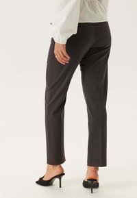 Donkergrijze op maat gemaakte broeken met een rechte snit, met een gladde textuur en zijsplitten aan de onderrand, gecombineerd met zwarte hoge hakken.