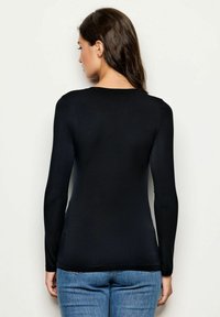 Schwarzes Langarmshirt aus weichem Stoff, mit rundem Ausschnitt und figurbetontem Schnitt. Getragen mit blauen Jeans.