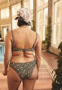 Divdaļīgs peldkostīms ar zaļu ziedu rakstu, kurā redzamas rozā puķes un sarkani augļi. Augšdaļai ir regulējamas lences un aizdare mugurpusē.