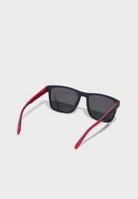 Ochelari de soare cu un cadru din plastic de culoare albastru marin, lentile întunecate și brațe texturate de culoare roșie. Formă pătrată, design ușor pentru confort.