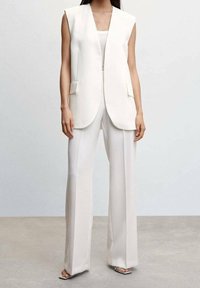 Bílá vesta bez rukávů s výstřihem do V a předními kapsami, kombinovaná s bílými kalhotami s vysokým pasem, které mají hladkou texturu a střihaný střih.