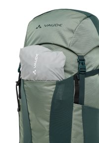La borsa Vaude verde presenta un esterno testurizzato, una tasca laterale con un sacchetto grigio chiaro e spallacci regolabili con dettagli in metallo.