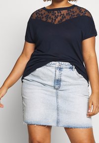 Marinblå t-shirt med blommönstrad meshnätöverdrag vid bröstet; kombinerad med en ljusblå denim mini kjol med fransad fåll och knappstängning fram.