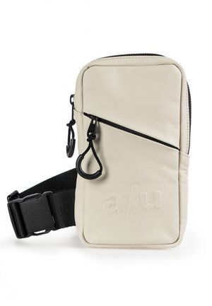 Kompakt beige crossbody taske med sort justerbar strop, diagonalt lynlås på frontlommen og prægede "a/u" logo på frontpanelet.