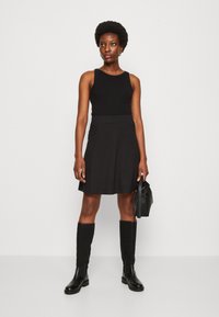 Un débardeur noir associé à une jupe évasée noire, des bottes noires jusqu'aux genoux et un petit sac à main noir, le tout sur un fond blanc.