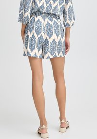 Pantaloni corti blu e beige con motivo, dotati di vita elastica e tasche laterali, realizzati in tessuto leggero. Lunghezza corta e vestibilità comoda.