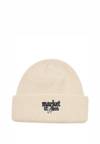 Strikket beige hue med en foldet kant, prydet med sort broderet tekst "market" og et lille grafisk element. Tekstureret stof med et varmt udtryk.