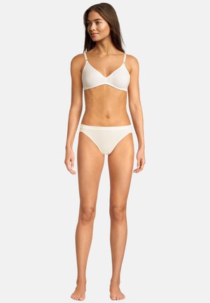 Woman standing barefoot wearing white seamless bra and matching panties on plain white background.