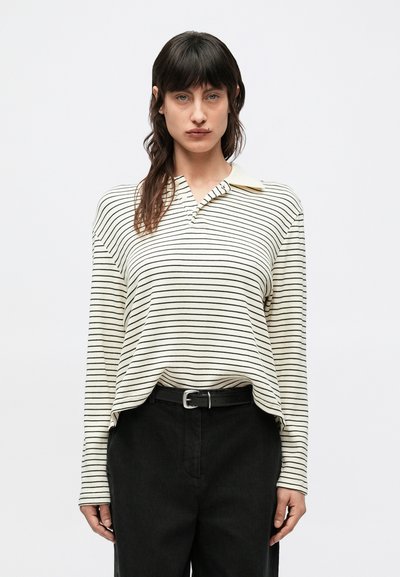 Haut à manches longues et col en crème avec des rayures noires. Présente une coupe décontractée et un tissu texturé. Associé à un pantalon noir taille haute.