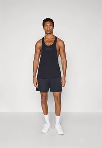 Must valge logoga varrukateta särk rinnal, kombineeritud tumedate lühikestega. Kandmisel valged spordijalatsid ja pahkluuni sokid.