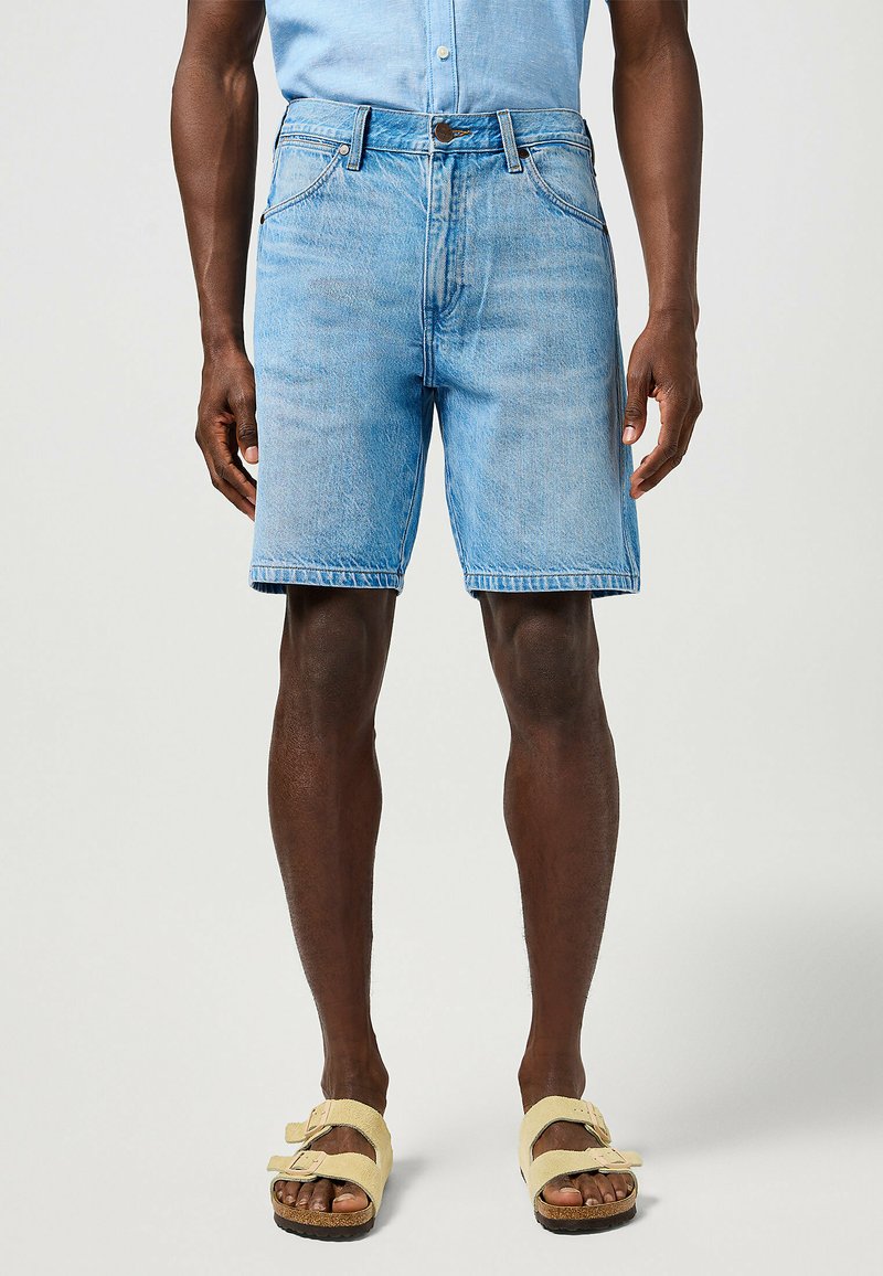 Jasnoniebieskie szorty dżinsowe o luznym kroju, pięć kieszeni i zapięcie na guzik. Noszone z żółtymi klapkami.